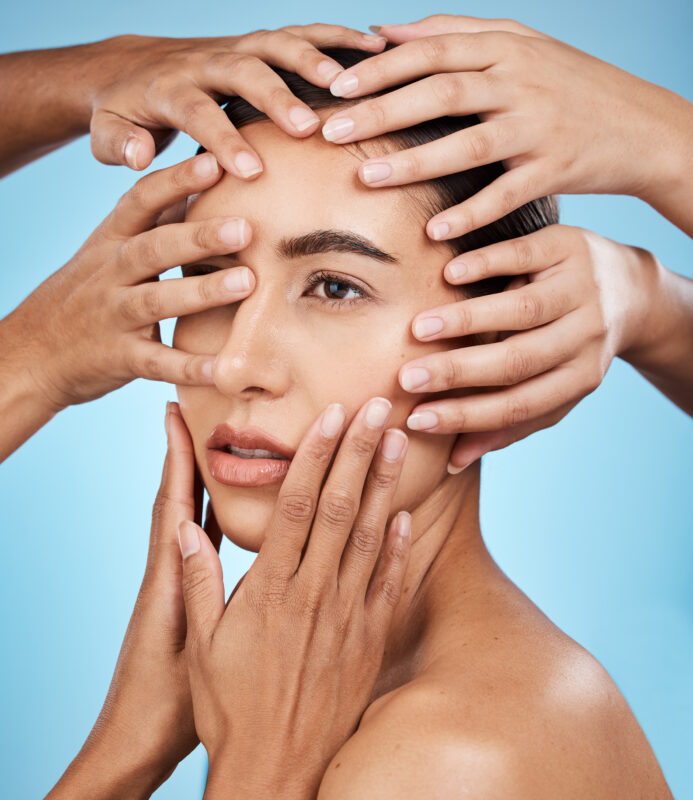 Close-up of a woman’s face surrounded by multiple hands gently touching her skin on a light blue background, symbolising skincare, facial firming, and skin tightening treatments.