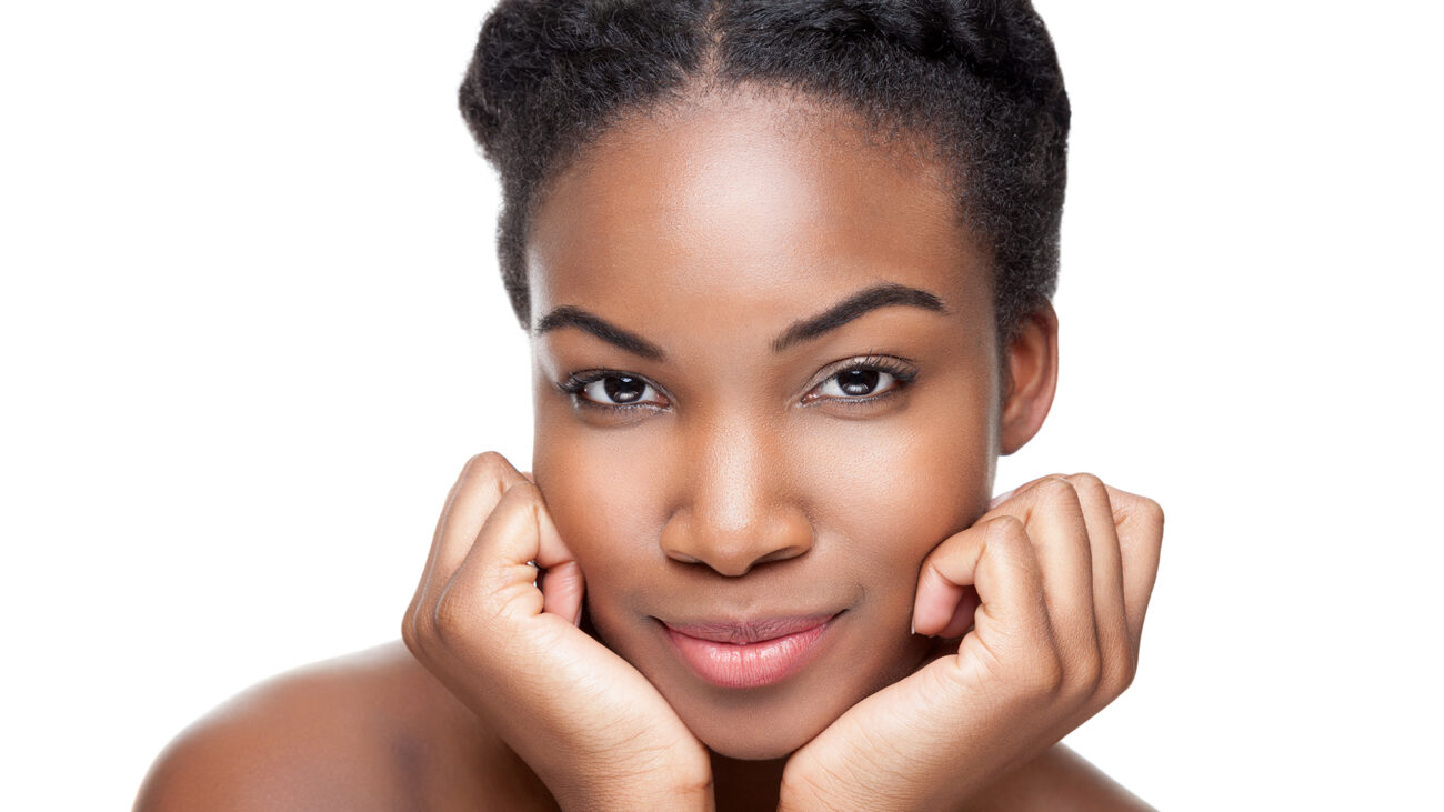 Woman with clear, healthy-looking skin resting her face on her hands against a white background