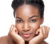 Woman with clear, healthy-looking skin resting her face on her hands against a white background
